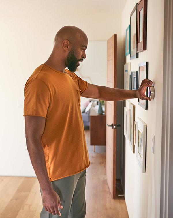 man in yellow shirt using thermostat in his house
